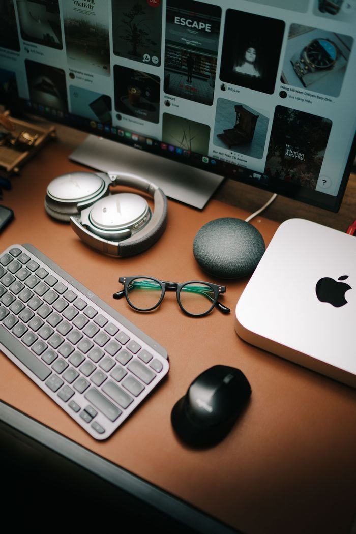 best-selling product-02 A stylish workspace featuring a keyboard, mouse, eyeglasses, headphones, and a screen displaying digital content.