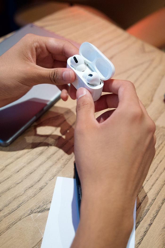 best-selling product-01 Person holding a pair of wireless earbuds in a case on a wooden table.